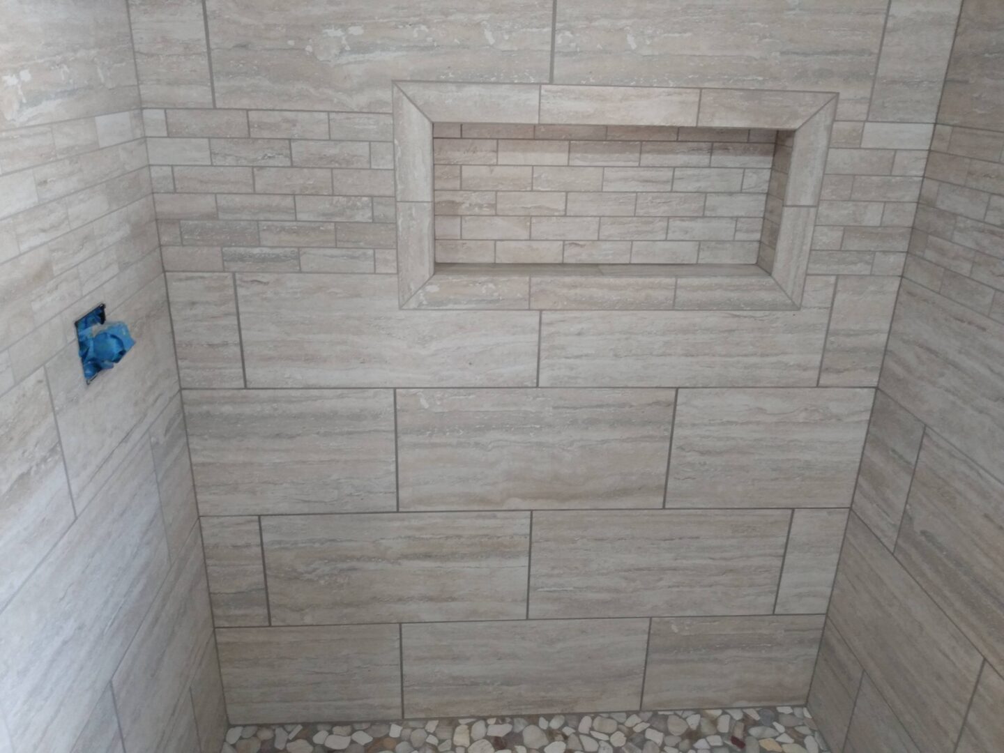 Portfolio image of a tile shower with 12x24" wall tiles, a recessed tile shelf, and small natural shaped tiles on the floor of the shower.
